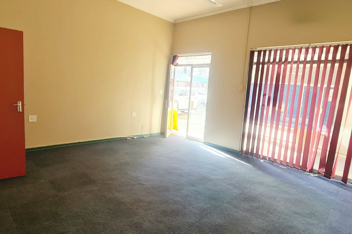 An empty office space featuring dark carpet flooring, vertical window blinds, and a glass panel door providing natural light.