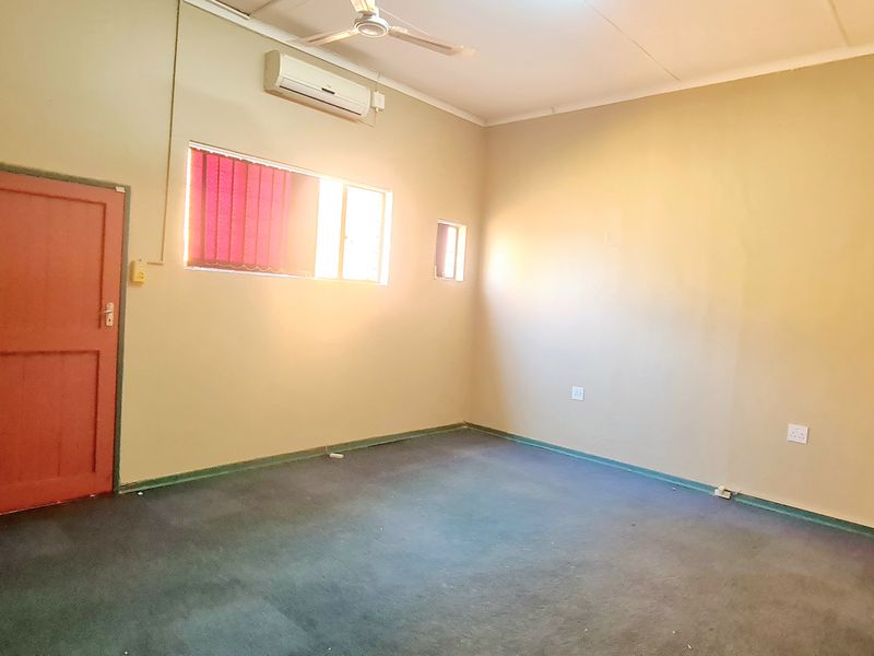 A vacant office space featuring carpeted flooring, a ceiling fan, and a wall-mounted air conditioning unit.