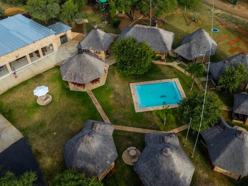 Aerial view of a farm property featuring multiple thatched-roof chalets, a central swimming pool, and landscaped grounds with paved pathways.