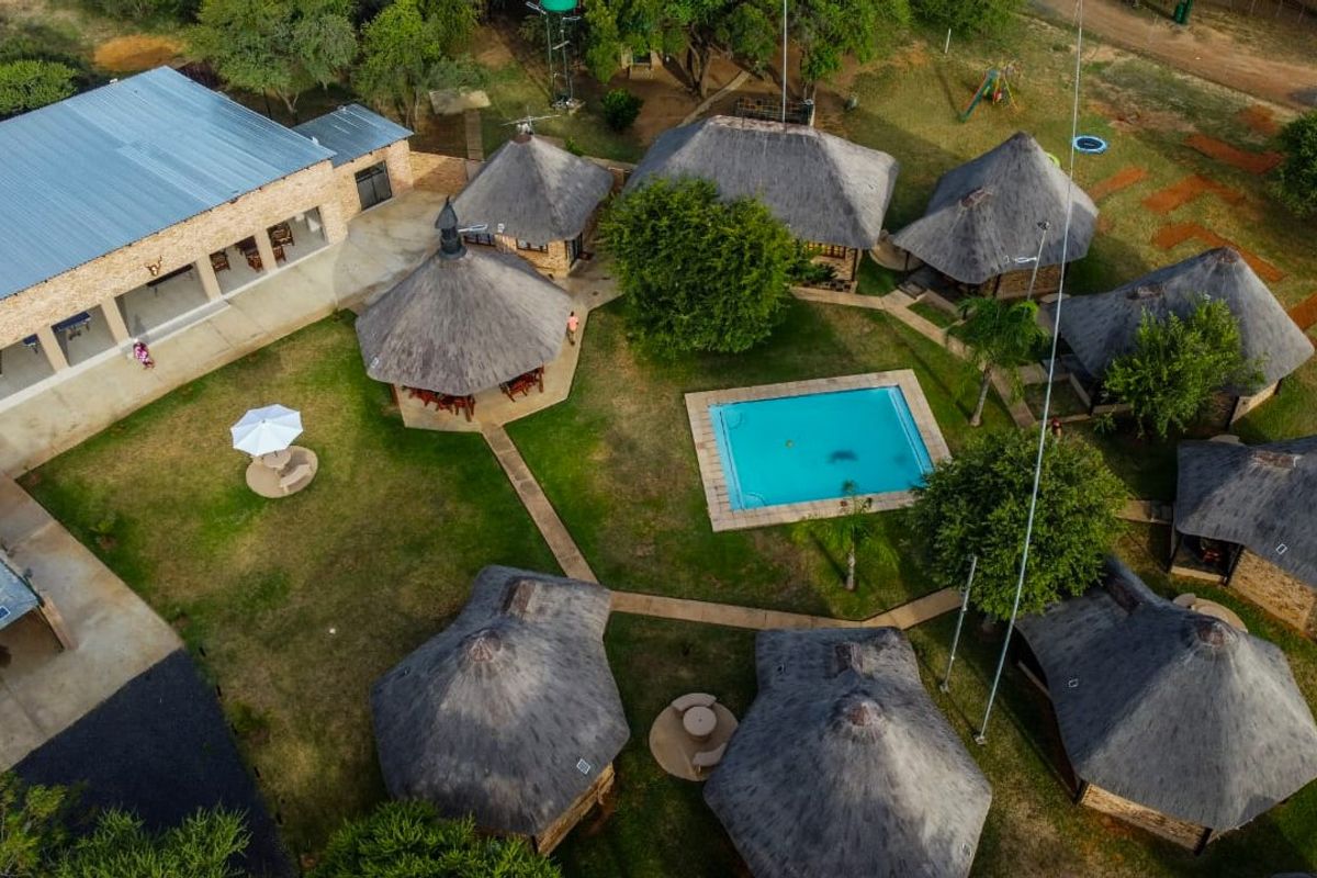 Aerial view of a farm property featuring multiple thatched-roof chalets, a central swimming pool, and landscaped grounds with paved pathways.