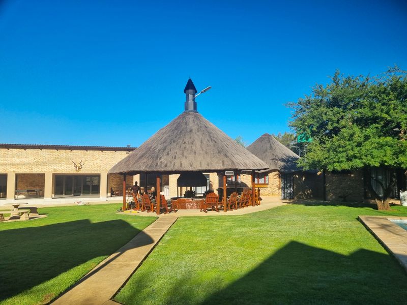 Spacious outdoor entertainment area featuring a traditional thatched lapa with a built-in braai, set within a well-maintained garden with paved pathways.