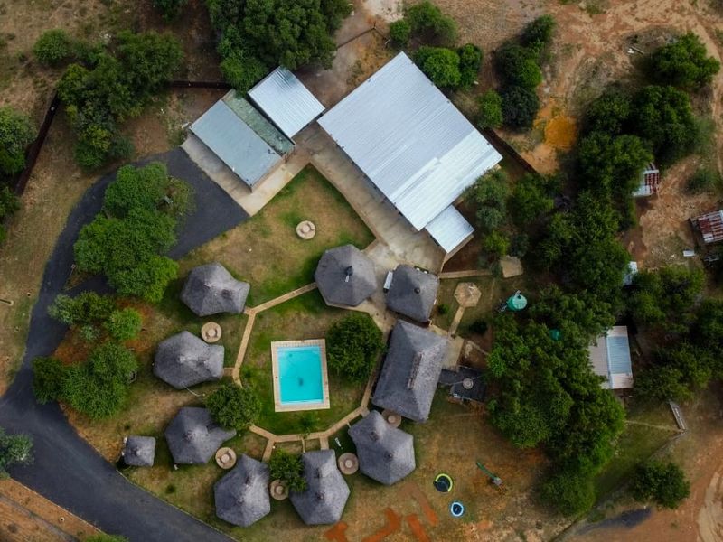 Aerial view of a farm property featuring multiple thatched-roof structures, a central swimming pool, a large metal-roofed shed, and surrounding landscaped grounds.