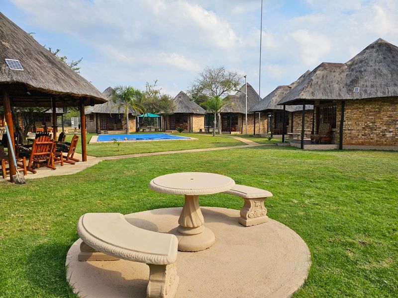 A well-maintained farm property featuring multiple thatched-roof cottages, a swimming pool, and landscaped garden areas with stone seating.