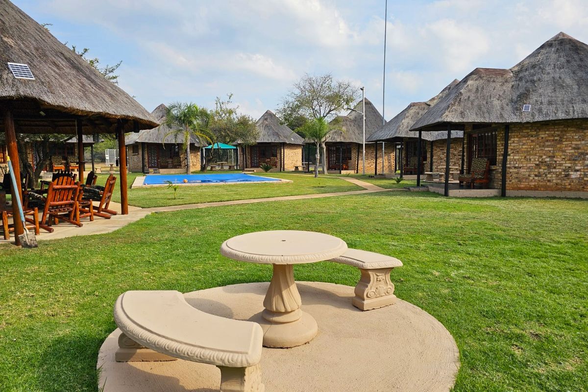 A well-maintained farm property featuring multiple thatched-roof cottages, a swimming pool, and landscaped garden areas with stone seating.