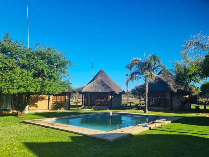 A well-maintained outdoor pool area featuring a swimming pool surrounded by lush green lawns and traditional thatched-roof structures.