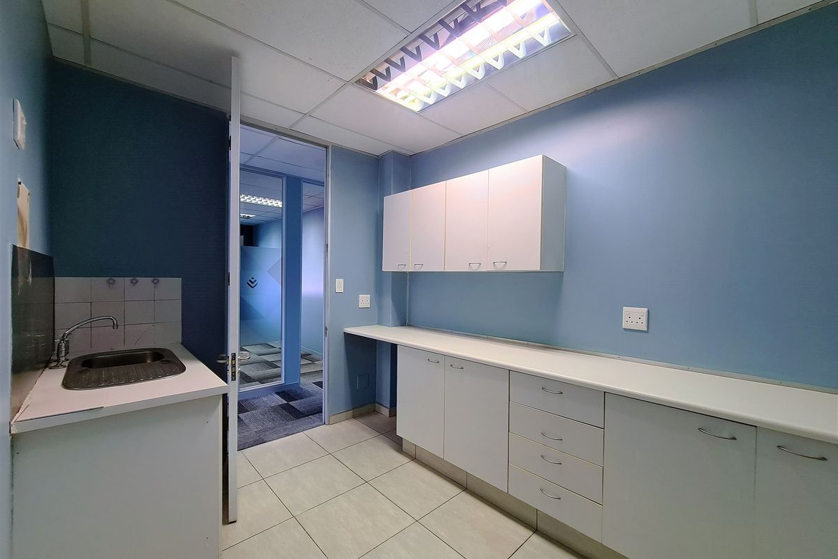 A functional office kitchenette featuring built-in white cabinetry, laminate countertops, a stainless steel sink, and tiled flooring with a drop ceiling.