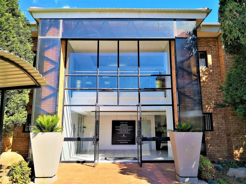 Modern office building entrance featuring a prominent glass facade, brick exterior, and a clear directory sign for the first-floor office suites.