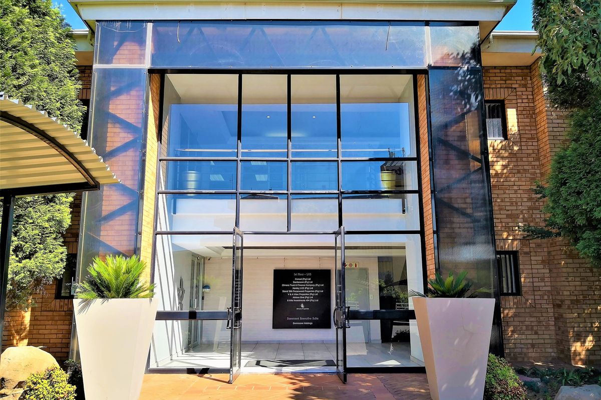 Modern office building entrance featuring a prominent glass facade, brick exterior, and a clear directory sign for the first-floor office suites.