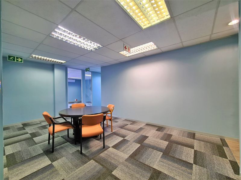 A functional office space featuring carpet tiles, suspended ceilings with recessed lighting, and clear signage for emergency exits.