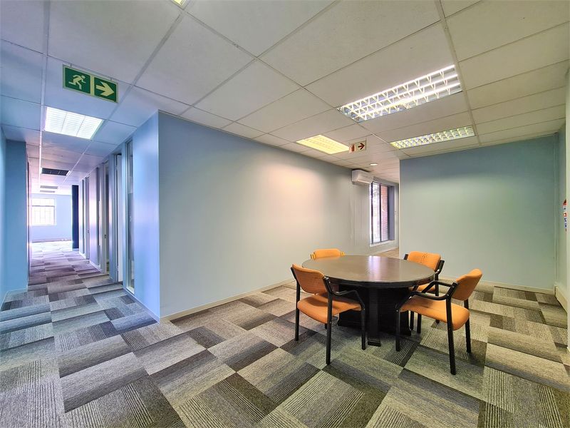 A professional office space featuring carpet tiles, suspended ceilings with recessed lighting, and glass partitions, providing a functional and well-lit work environment.