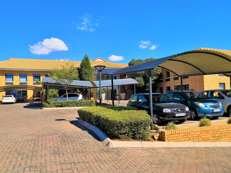 Front view of the office building featuring a paved parking area with covered bays and established garden landscaping.