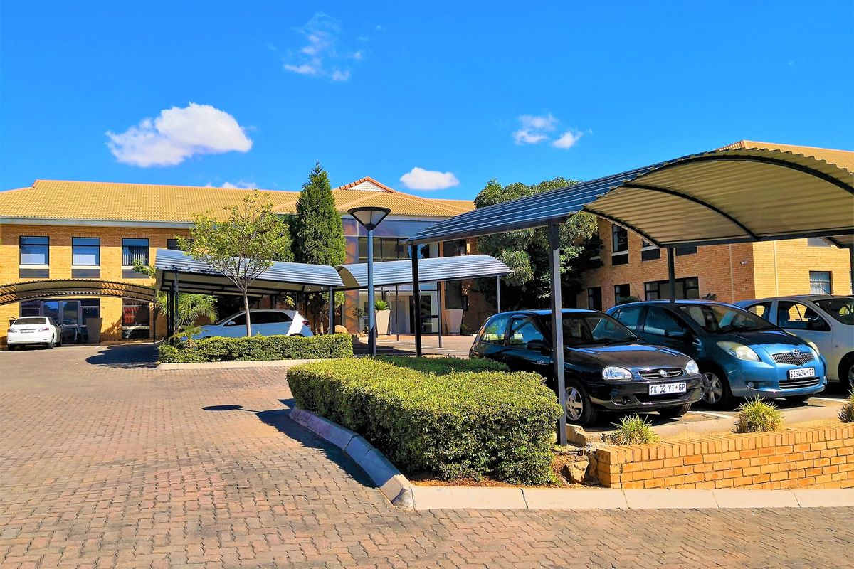 Front view of the office building featuring a paved parking area with covered bays and established garden landscaping.