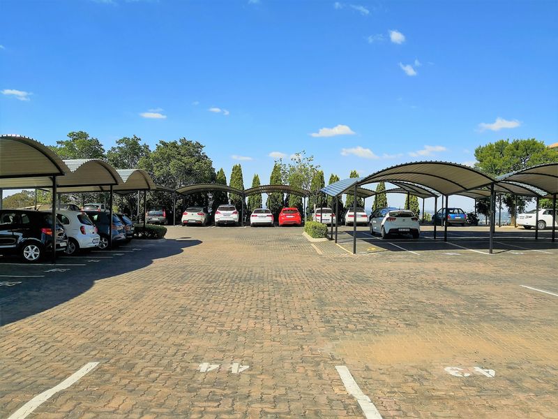 Outdoor paved parking area featuring multiple covered parking bays with metal roofing structures.