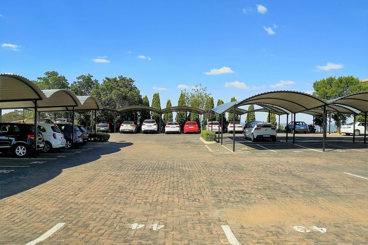 Outdoor paved parking area featuring multiple covered parking bays with metal roofing structures.