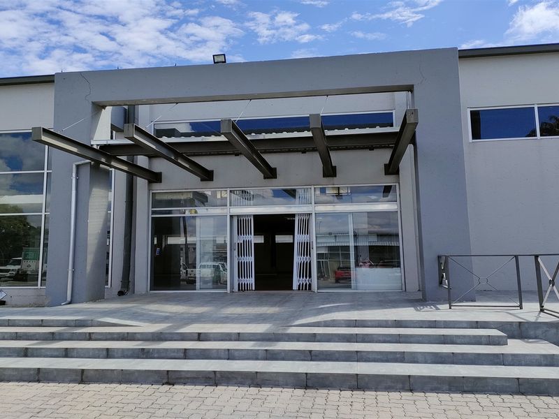Front entrance of an industrial building featuring a modern steel cantilevered canopy, glass sliding doors, and wide stone-paved steps.