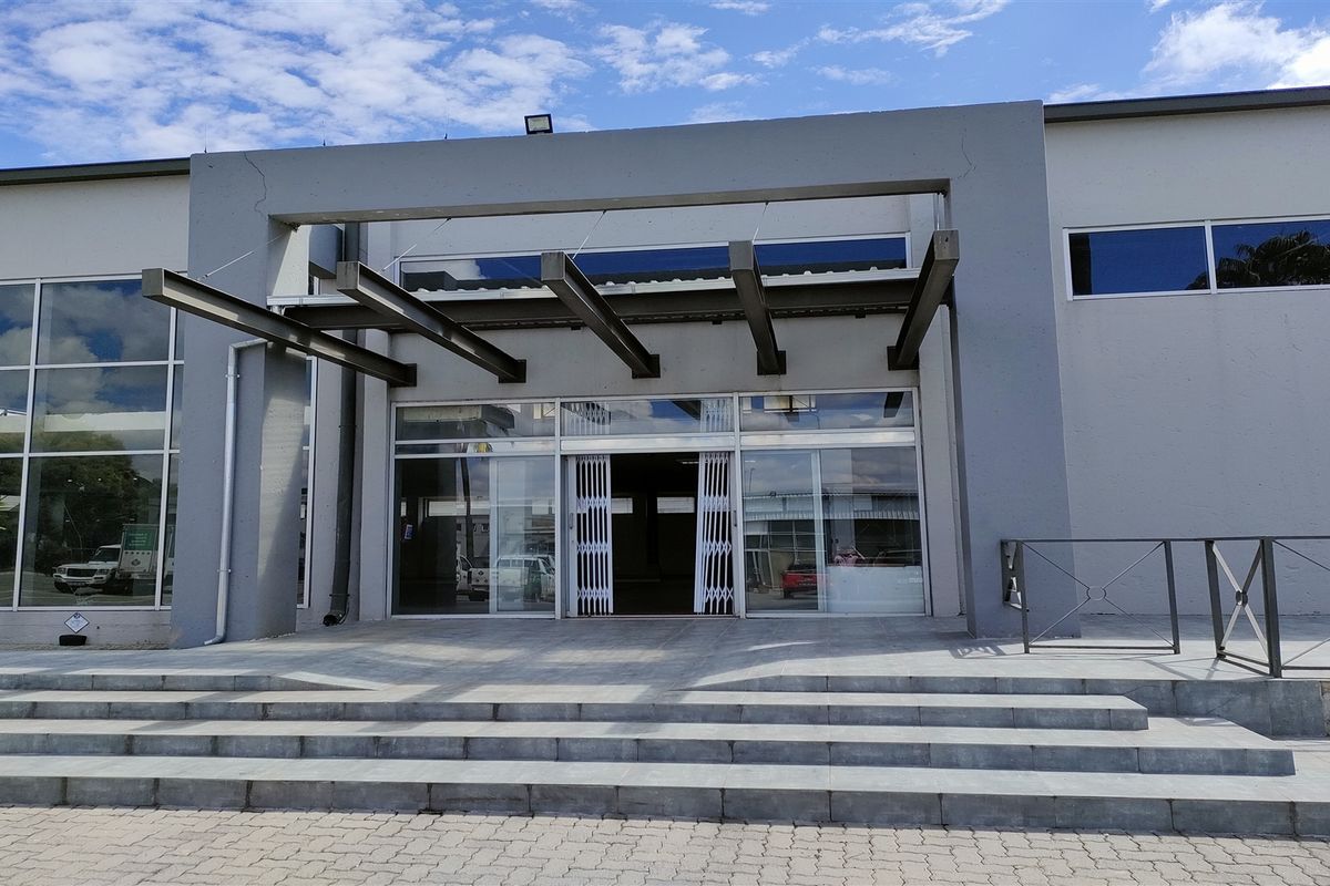 Front entrance of an industrial building featuring a modern steel cantilevered canopy, glass sliding doors, and wide stone-paved steps.