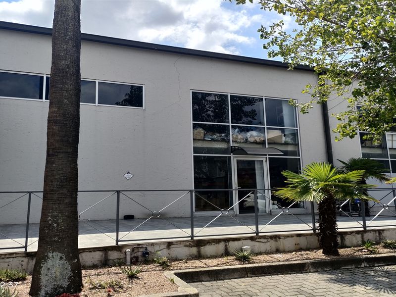 Front elevation of an industrial property featuring a tiled patio, metal railing, and large glass facade with an entrance door.