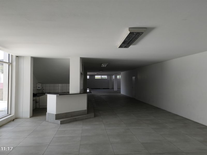 Spacious open-plan industrial unit featuring tiled flooring, structural columns, fluorescent lighting, and a small kitchenette area with a security gate at the entrance.