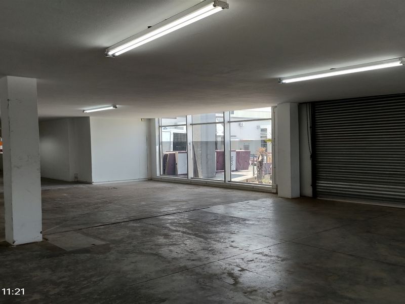 Spacious industrial utility area featuring concrete flooring, fluorescent lighting, and a large roller shutter door with expansive glass windows.