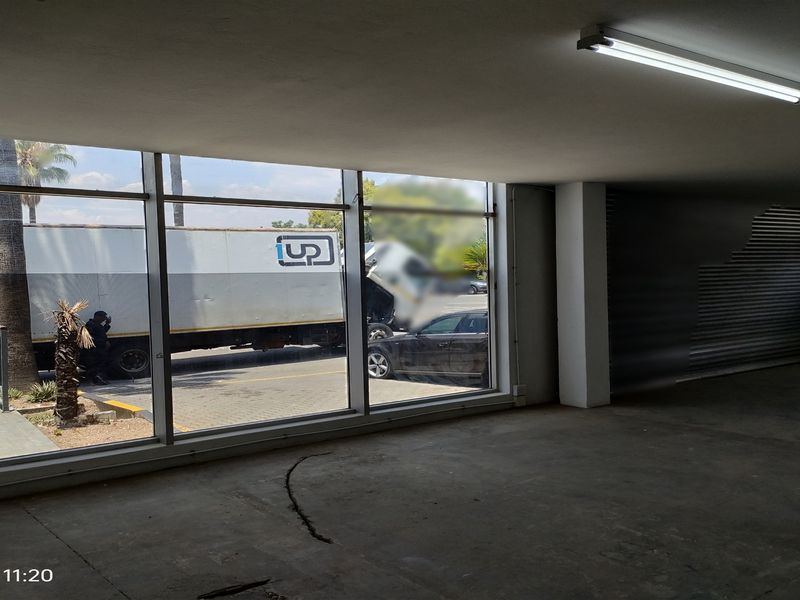 An empty industrial office space featuring large glass windows, concrete flooring, and a roller shutter door, suitable for commercial or warehouse use.