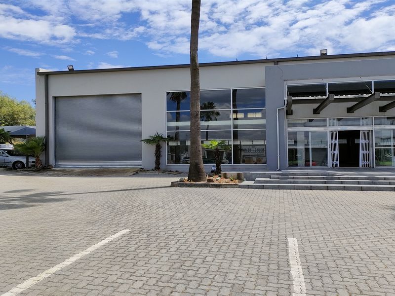 Front elevation of an industrial property featuring a large roller shutter door, expansive glass facade, and a paved parking area.