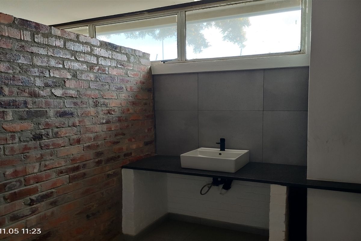 A modern industrial-style bathroom featuring an exposed brick wall, a vessel sink with a black faucet, and a stone countertop.