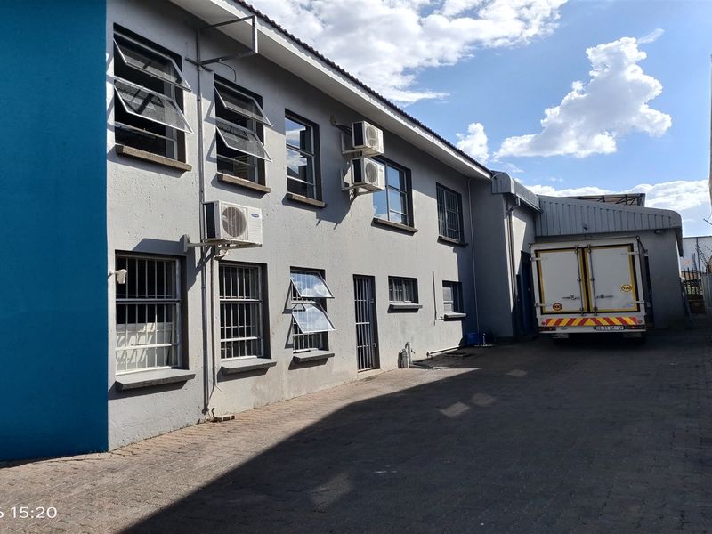 Rear exterior view of the industrial property featuring a paved driveway, security bars on windows, and wall-mounted air conditioning units.