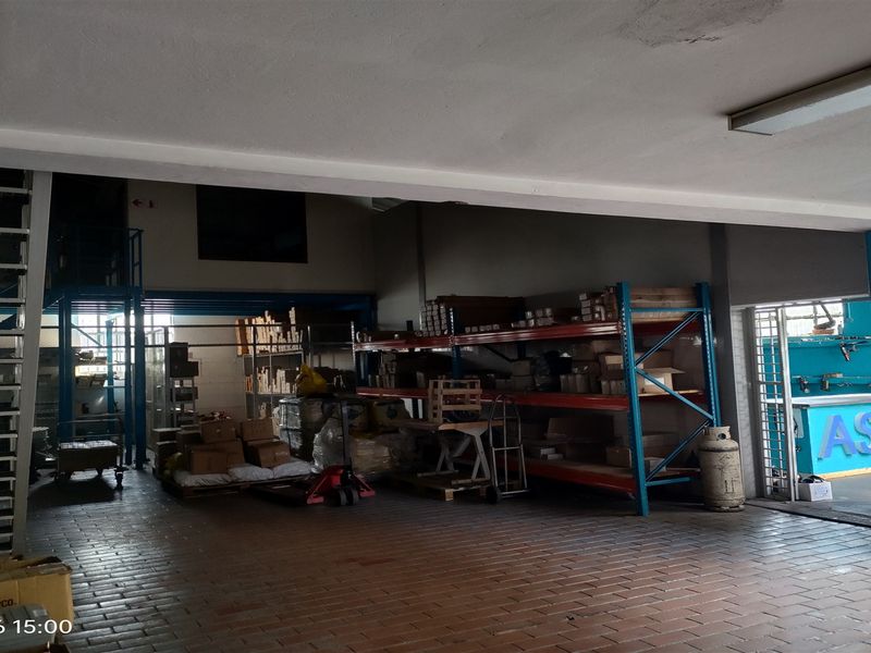 Industrial warehouse space featuring a mezzanine level, steel staircase, heavy-duty shelving units, and durable brick flooring with a secure entrance.