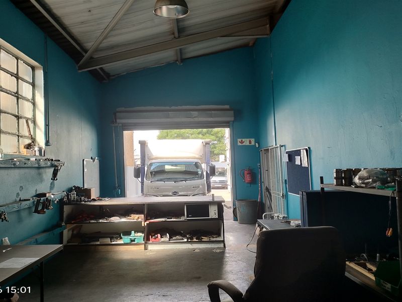 Industrial utility space featuring exposed steel roof trusses, concrete flooring, and a large roller shutter door providing direct access for vehicles.