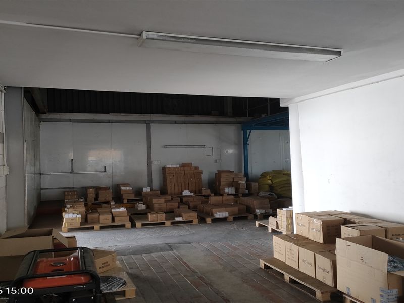 Industrial utility or storage space featuring concrete flooring, tiled wall sections, and overhead fluorescent lighting, currently utilized for inventory storage.