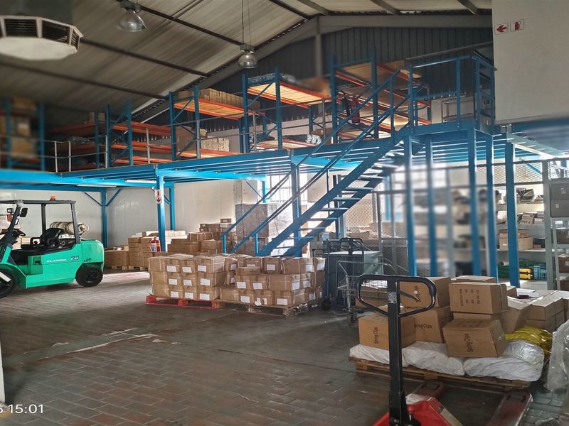 Spacious industrial warehouse area featuring a steel mezzanine level, staircase, and extensive racking systems suitable for storage and logistics operations.