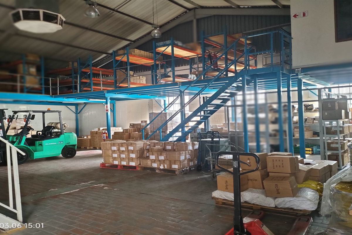 Spacious industrial warehouse area featuring a steel mezzanine level, staircase, and extensive racking systems suitable for storage and logistics operations.