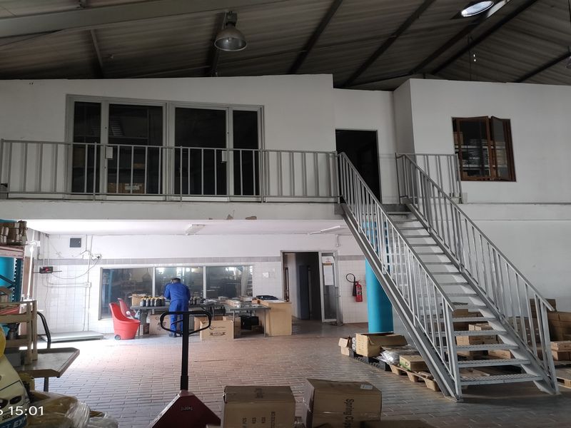 Industrial warehouse space featuring a mezzanine level with metal staircase, high ceilings, and functional tiled flooring suitable for storage or office operations.