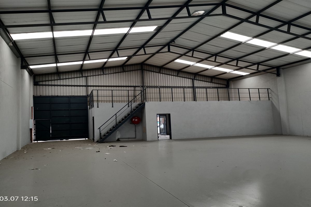 Spacious industrial warehouse featuring a high-clearance roof with skylights, a mezzanine level with metal railing, and a large roller shutter door.
