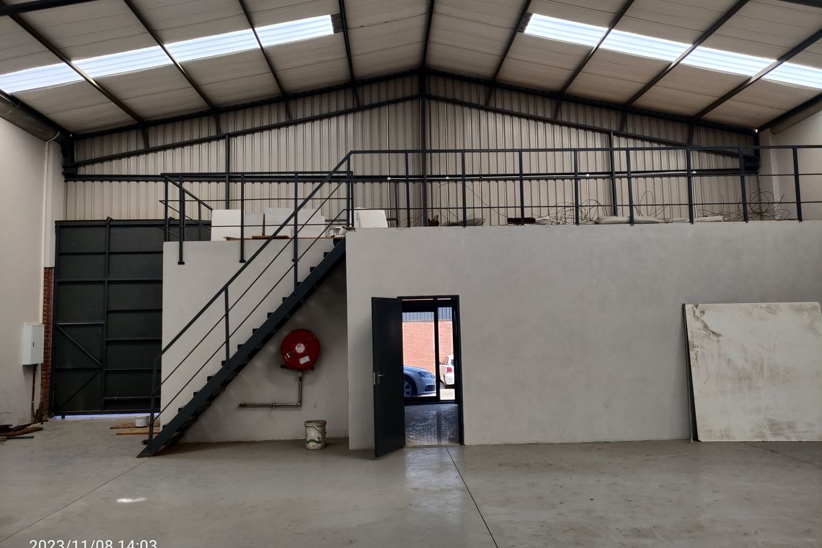 Industrial warehouse space featuring a mezzanine level with metal staircase, high-pitched roof with skylights, and concrete flooring.