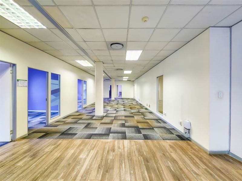 Spacious open-plan office area featuring a mix of carpet and wood-look flooring, suspended ceilings with recessed lighting, and internal glass-partitioned office rooms.