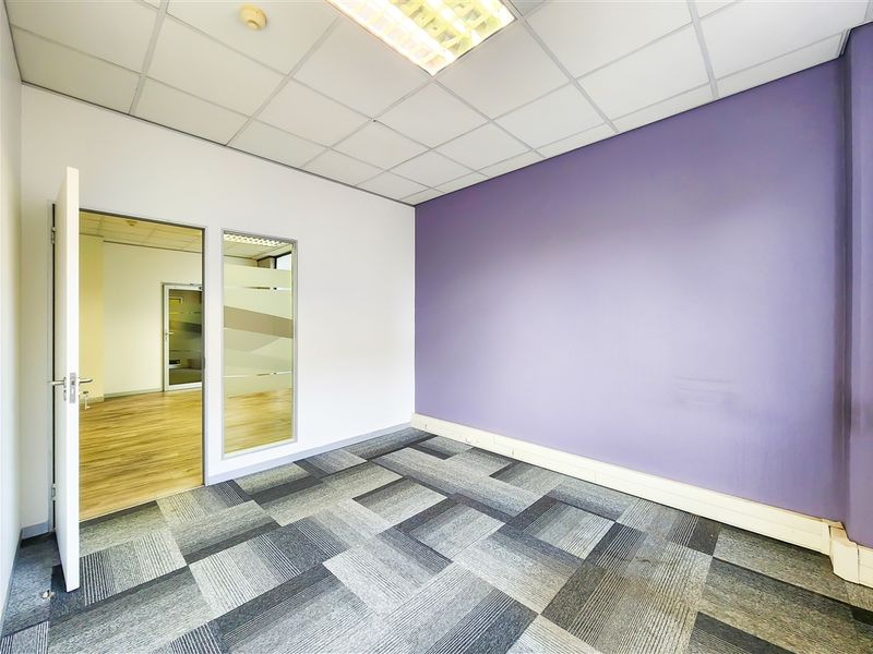 A vacant office space featuring carpet tiles, a suspended ceiling with recessed lighting, and a glass partition wall.