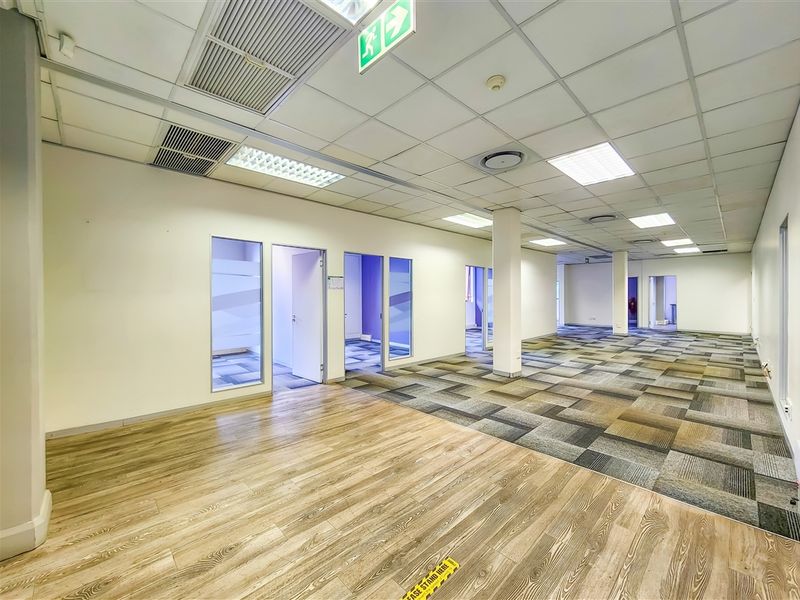 Spacious open-plan office area featuring a mix of wood-look vinyl and carpet tile flooring, suspended ceilings, and multiple private partitioned office rooms.