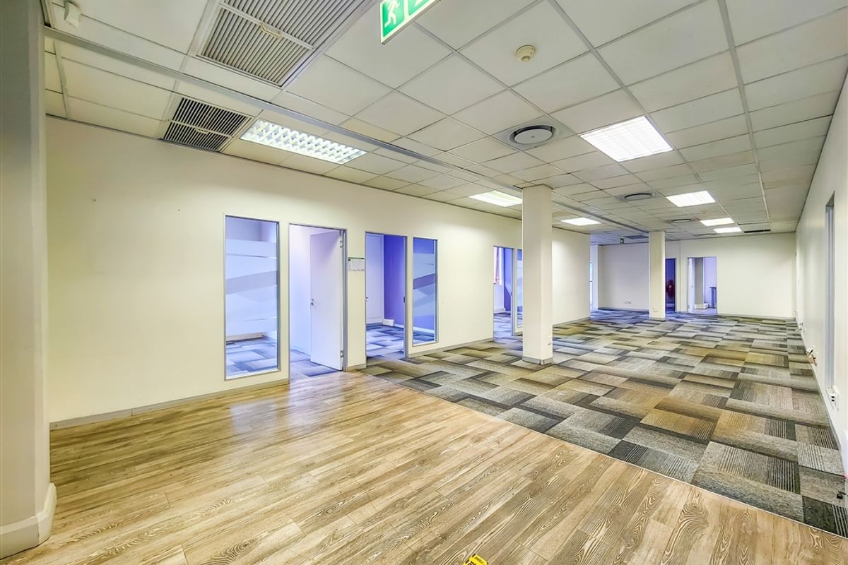 Spacious open-plan office area featuring a mix of wood-look vinyl and carpet tile flooring, suspended ceilings, and multiple private partitioned office rooms.