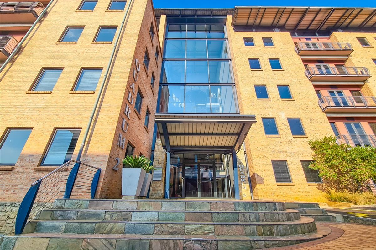 Front elevation of a multi-story office building featuring a prominent glass atrium entrance, brick facade, and stone staircase access.