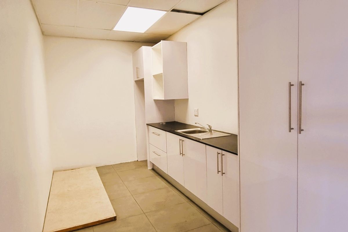 A compact office kitchenette featuring white cabinetry, a dark countertop, a stainless steel sink, and tiled flooring.