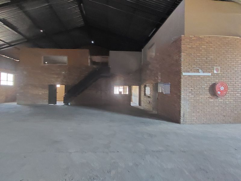 Spacious industrial utility area featuring exposed brick walls, high metal roof structure, and concrete flooring, suitable for warehouse or workshop use.