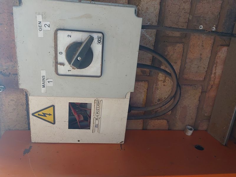 Industrial electrical changeover switch mounted on a brick wall, showing signs of wear and exposed wiring.