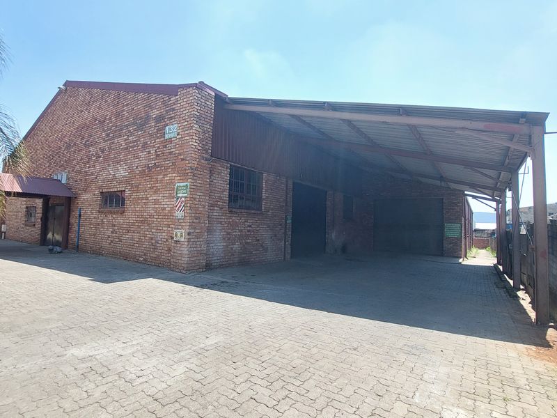 Industrial property featuring an exposed brick facade, a large covered loading area, and a paved driveway with secure boundary walling.