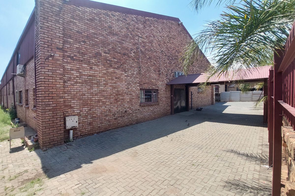 Rear exterior view of an industrial property featuring a face brick facade, paved driveway, and a covered walkway entrance.