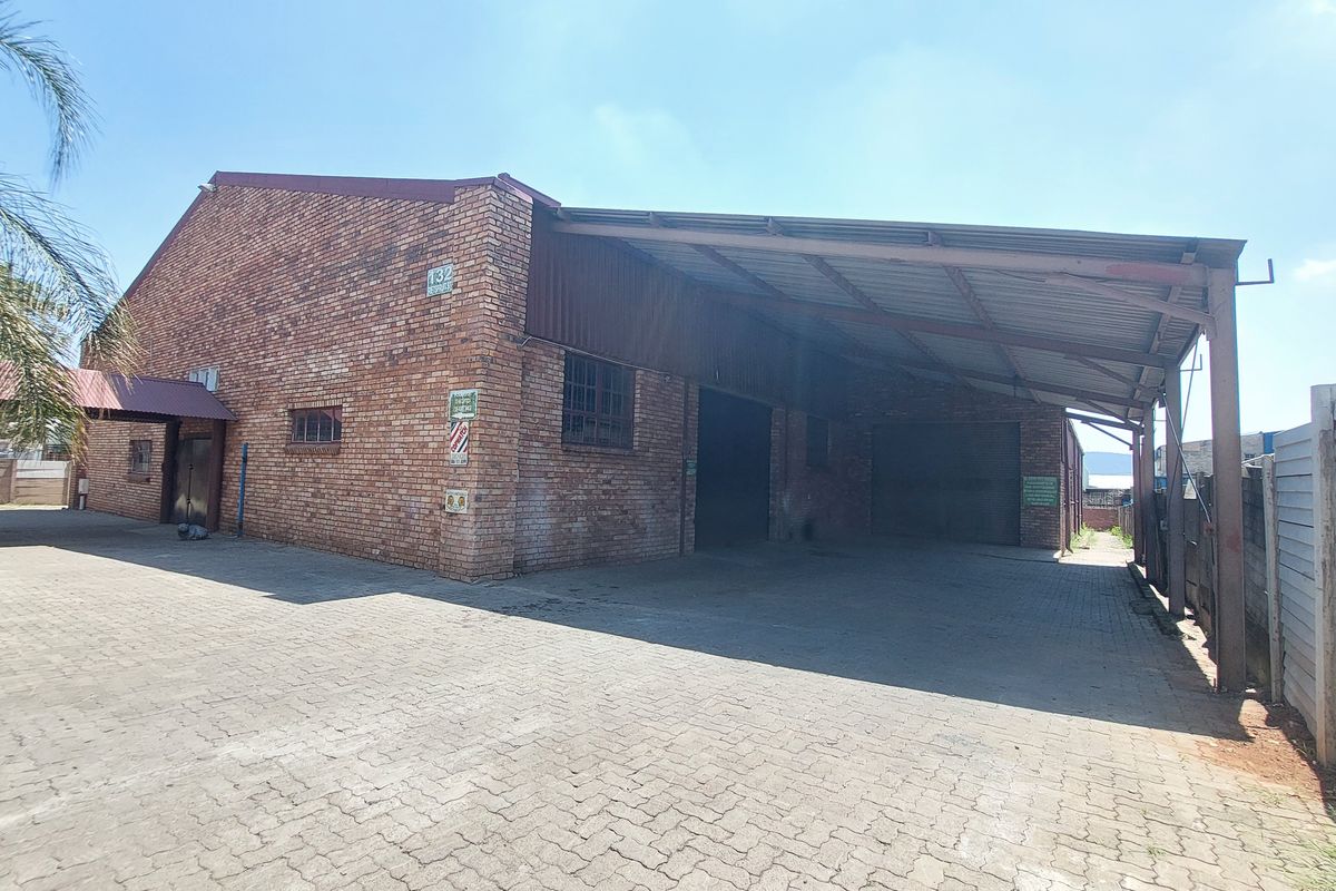 Industrial property featuring an exposed brick facade, a large covered loading area, and a paved driveway with secure boundary walling.