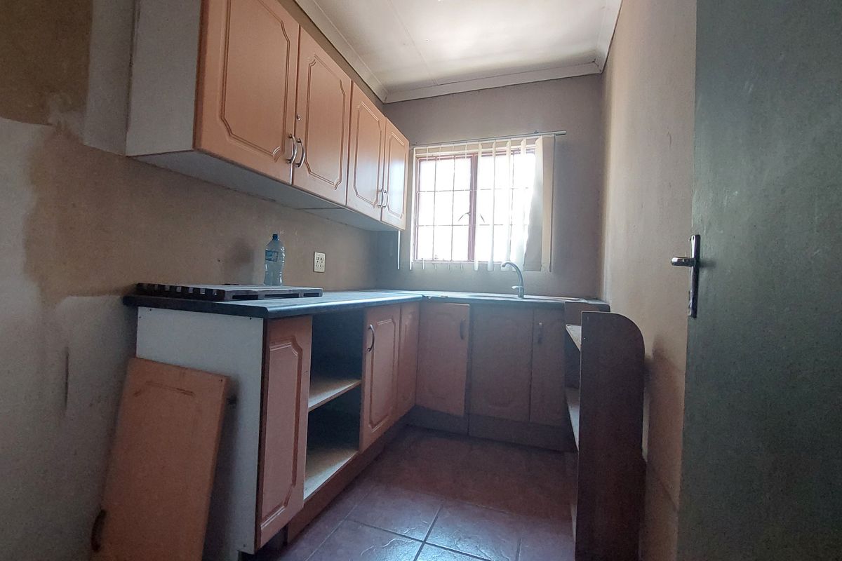 A small, dated kitchen featuring laminate cabinetry, a stainless steel sink, and tiled flooring, currently in need of renovation and cosmetic repairs.