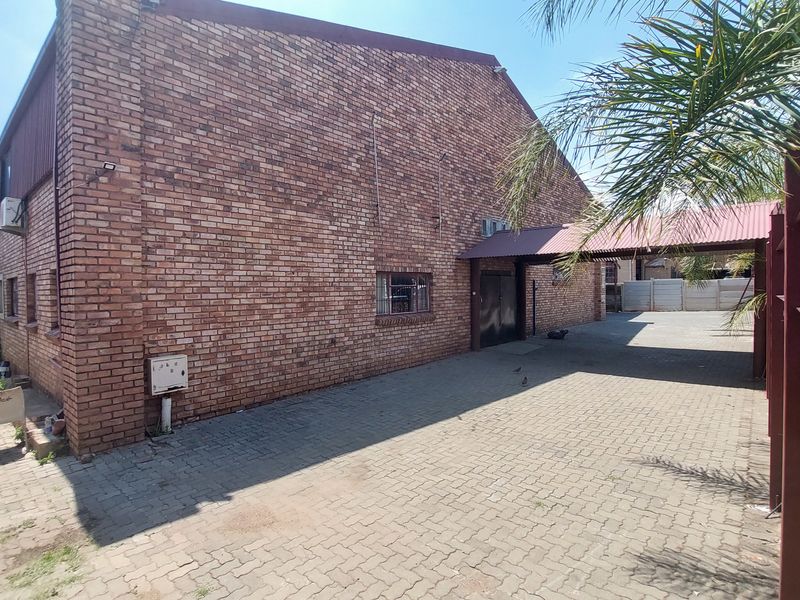 Rear exterior view of an industrial property featuring a face brick facade, paved driveway, and a covered walkway entrance.