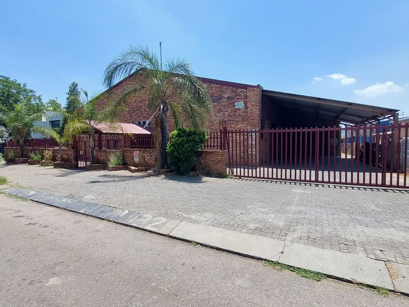 Front exterior view of an industrial property featuring a brick facade, secure metal gate, and a paved driveway with a covered loading area.