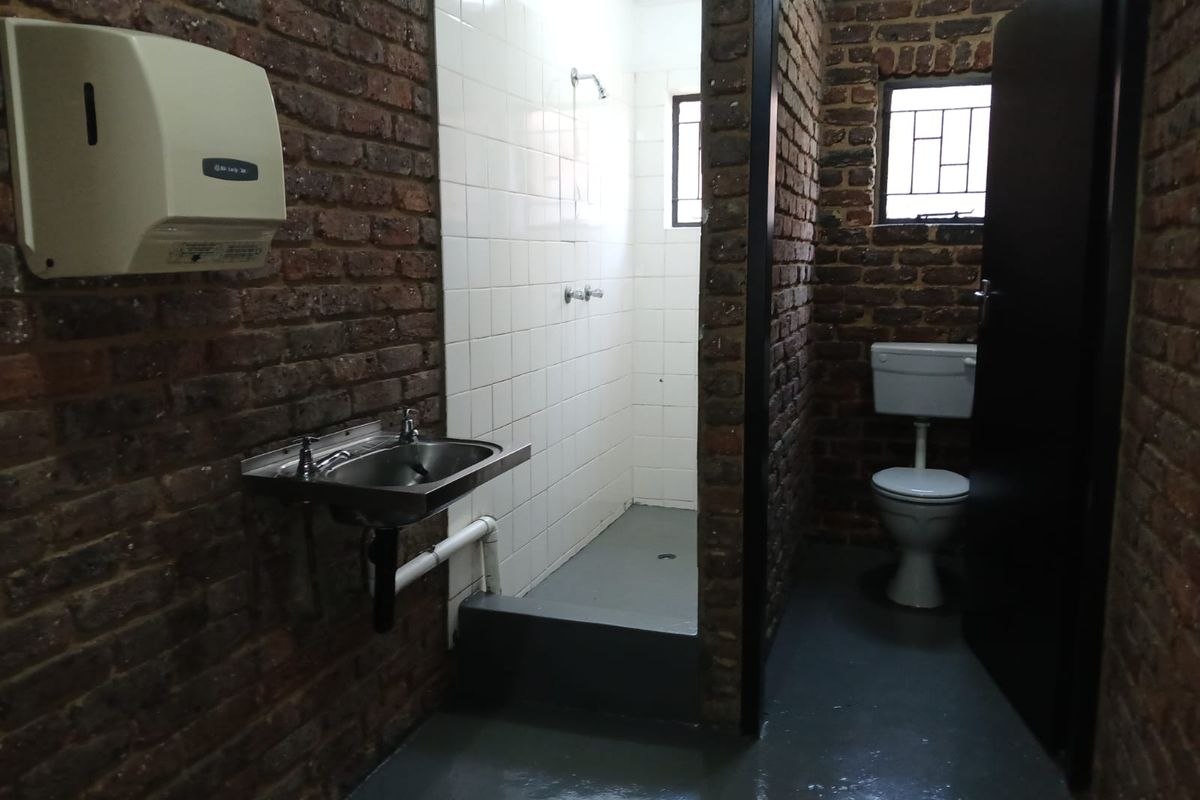 Industrial-style bathroom featuring exposed brick walls, a stainless steel basin, a walk-in shower, and a separate toilet cubicle.